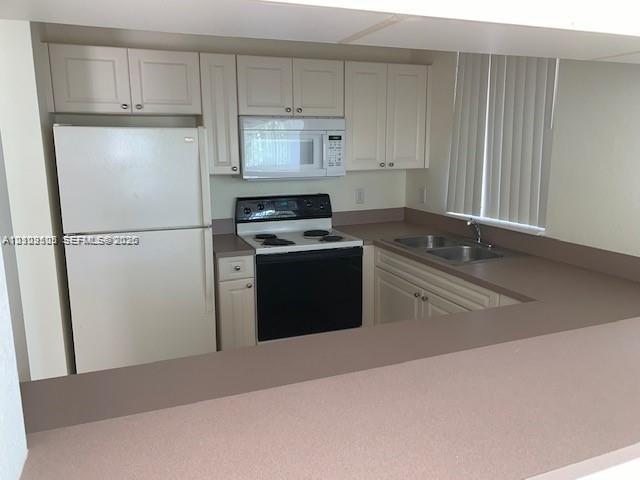 Kitchen featuring white cabinetry, solid-surface countertops, dual-basin sink, and white appliances including a built-in microwave and range