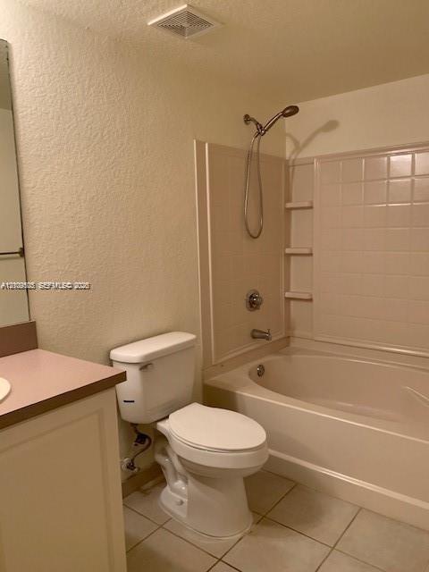 Bathroom featuring a vanity with a solid-surface countertop, a porcelain toilet, and a combination tub and shower enclosure with integrated shelving and a handheld showerhead