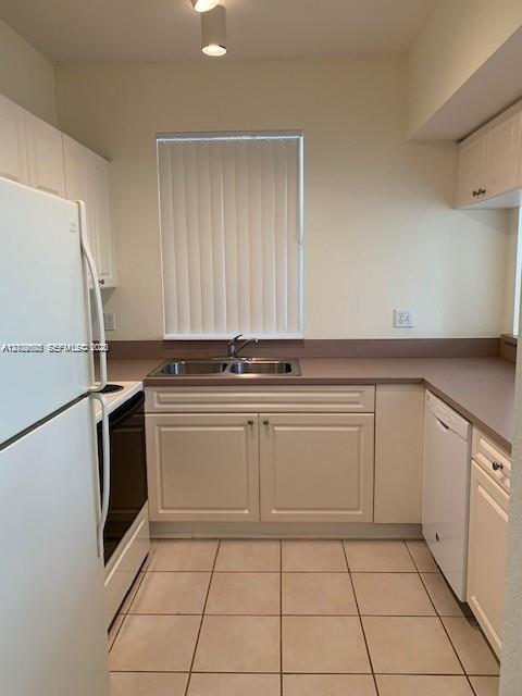 Kitchen featuring white cabinetry, solid-surface countertops, dual-basin stainless steel sink, tiled flooring, and white appliances