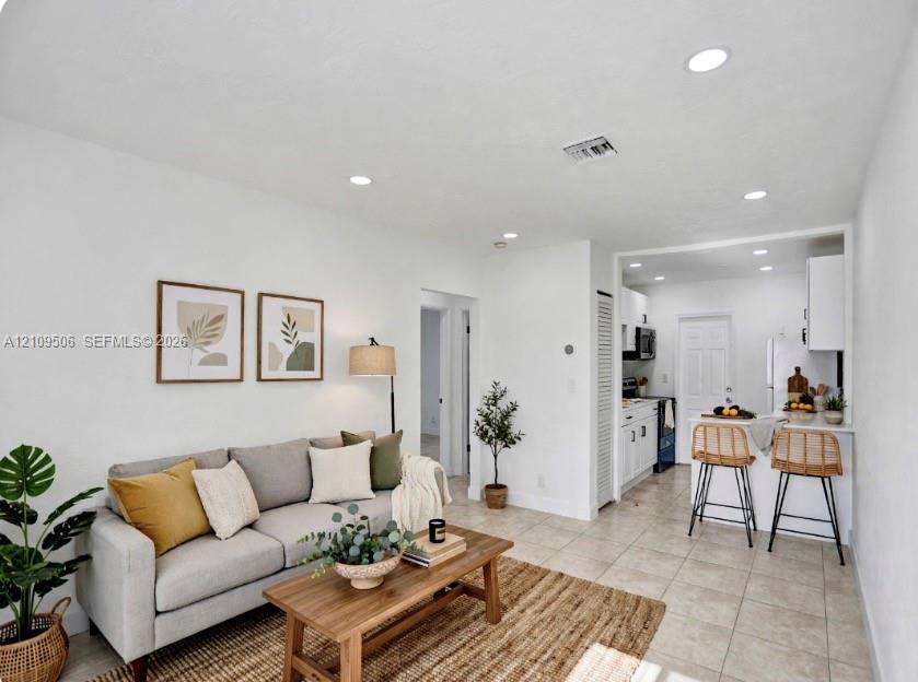 Staged space featuring neutral tile flooring, recessed lighting, and a breakfast bar with stone-finish countertop