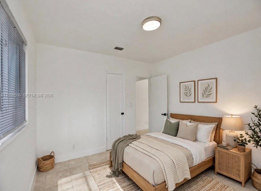 Staged interior space featuring tile flooring, a flush-mount ceiling light fixture, a window with horizontal blinds, and solid-core interior doors with matte black hardware