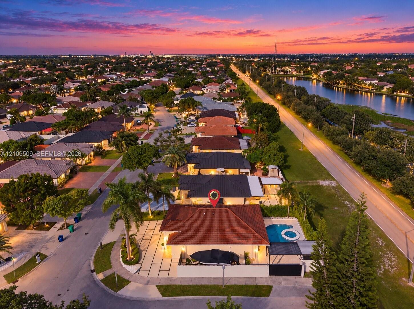 Aerial perspective of a corner-lot property featuring a tile roof, an integrated swimming pool and spa, a paved driveway with turf accents, and perimeter wall fencing
