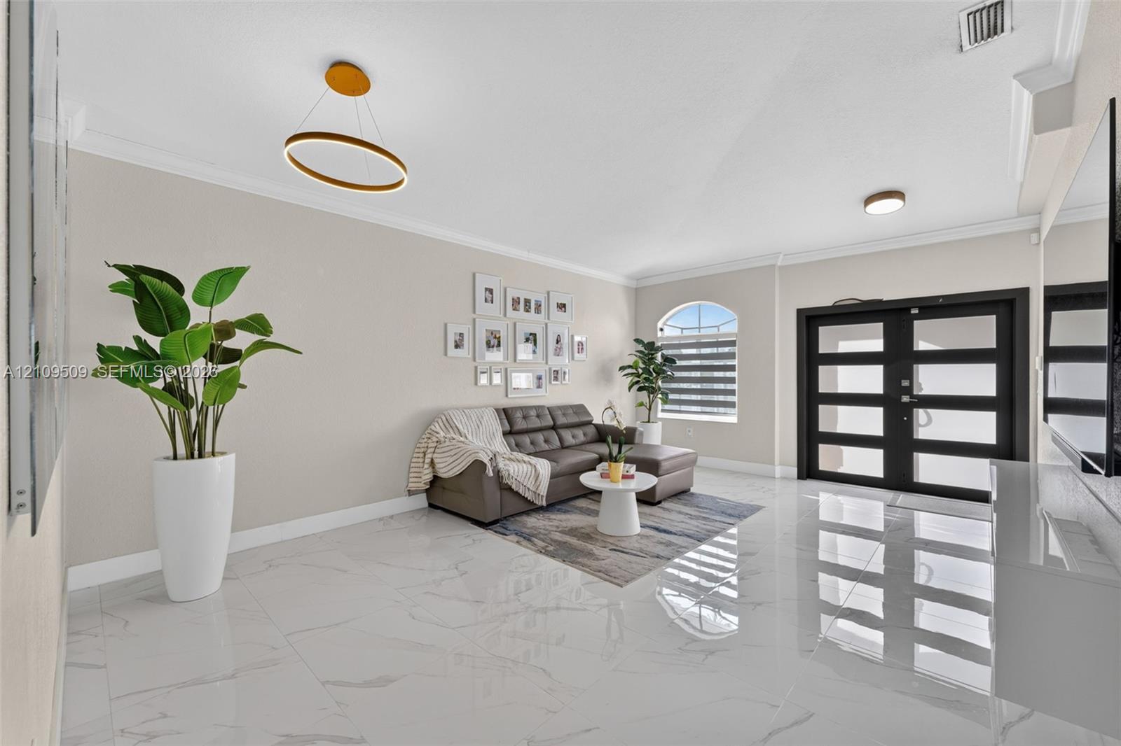 Large-format polished tile flooring, double-door entry with glass panels, crown molding, modern ring-style pendant lighting, and an arched window