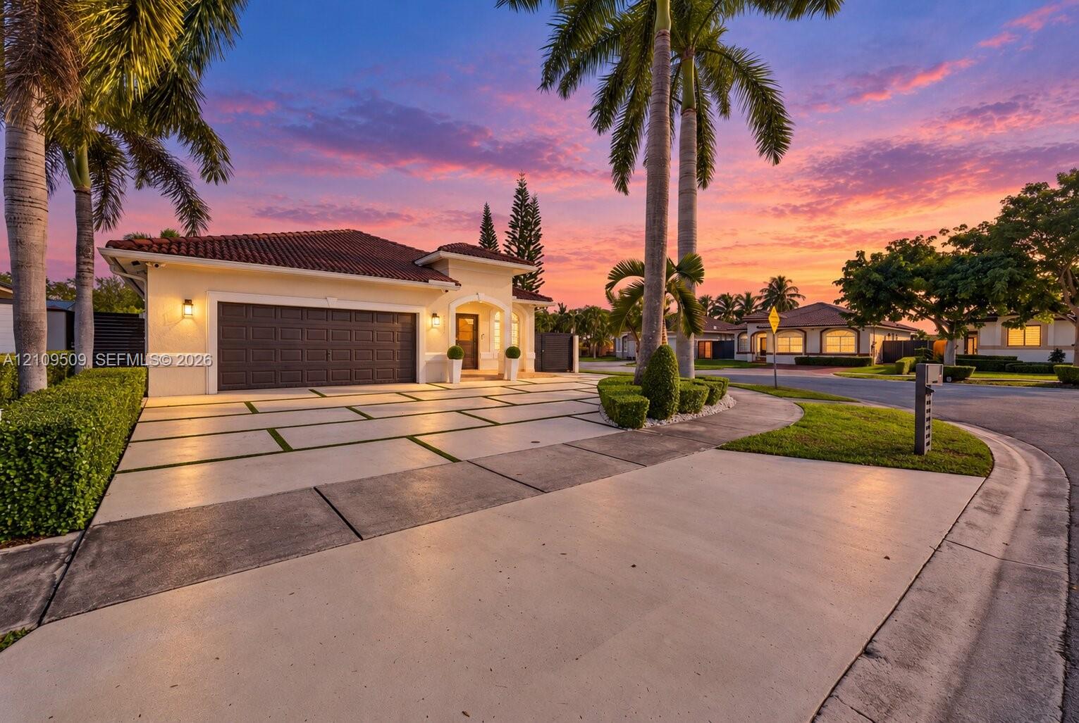 Stucco exterior residence with a multi-piece tile roof, featuring a grid-pattern concrete driveway with grass insets, mature palm trees, and manicured landscaping