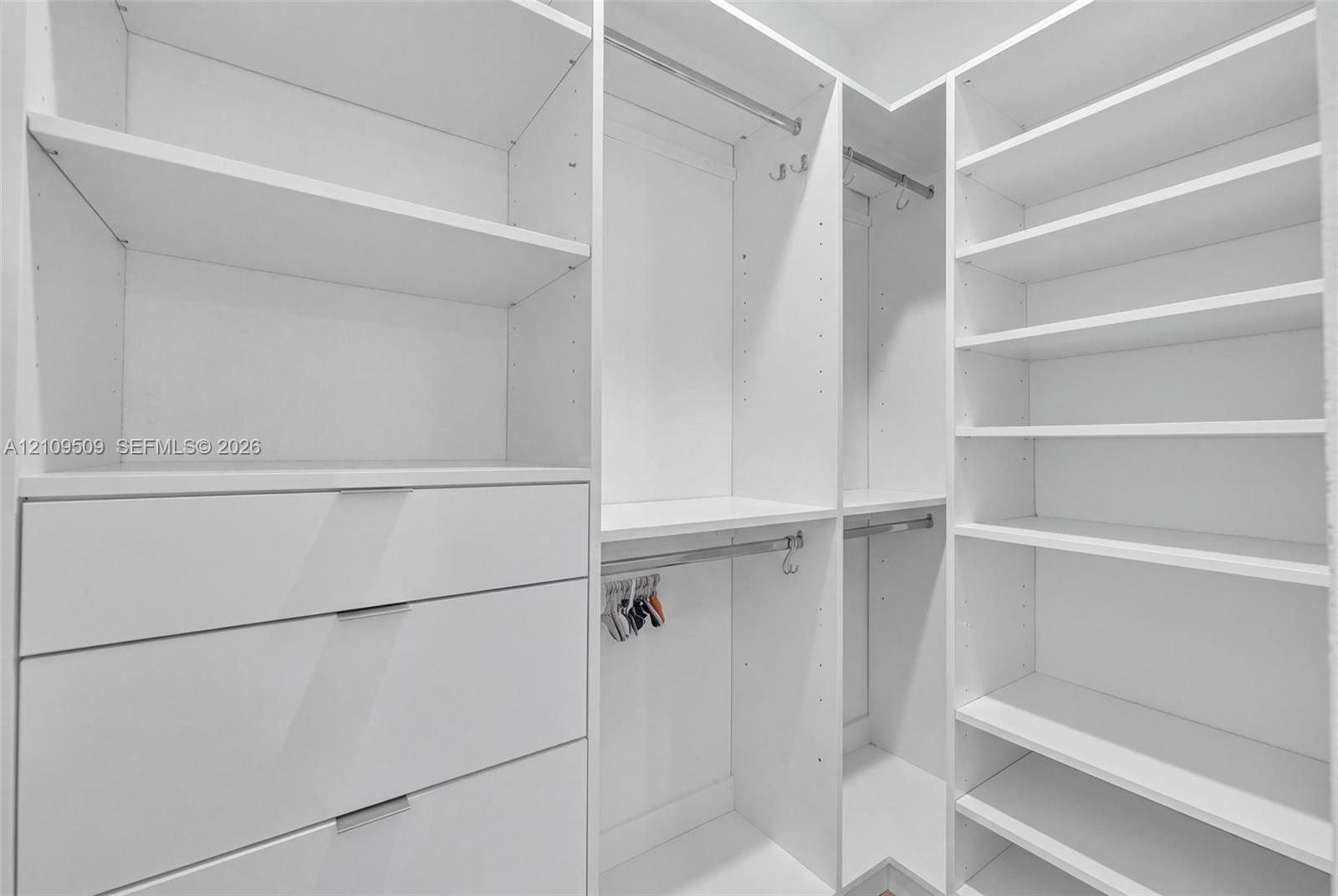 Custom walk-in closet featuring white built-in shelving, integrated dresser drawers, double hanging rods, and adjustable rack hardware