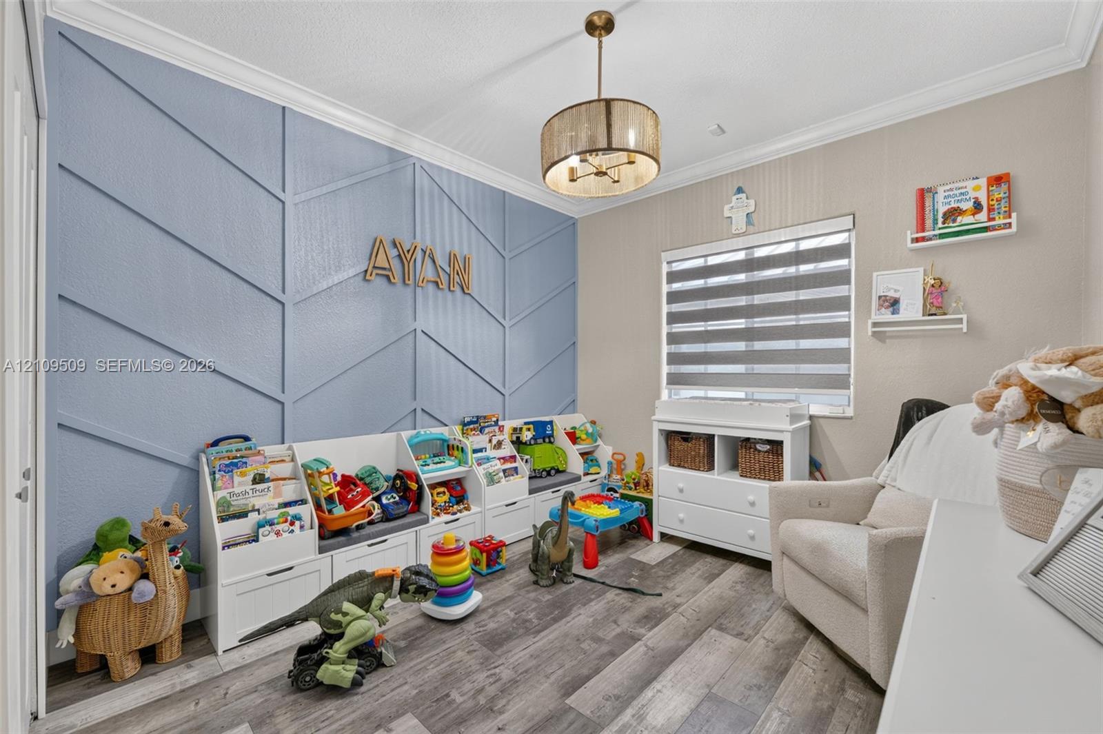 Accent wall with decorative geometric molding, wood-finish flooring, crown molding, drum pendant light fixture, and horizontal window shades