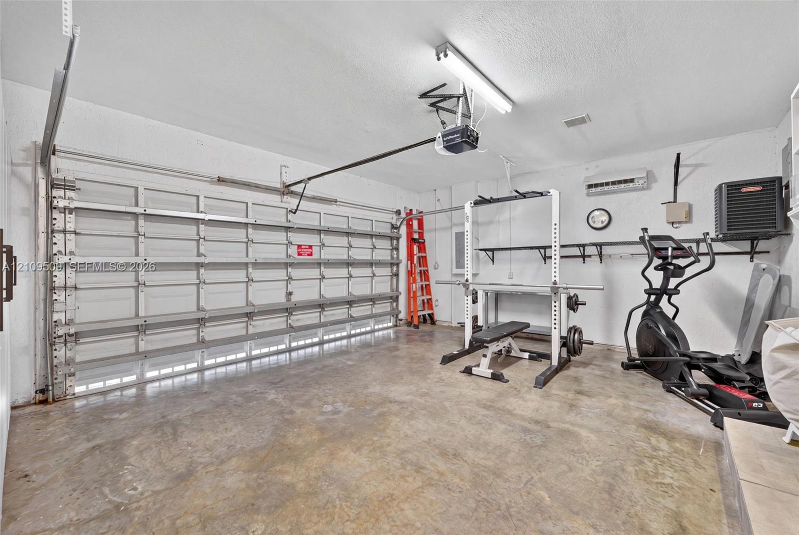 Multi-car garage featuring a concrete floor, motorized sectional garage door, wall-mounted ductless mini-split system, and built-in wall shelving