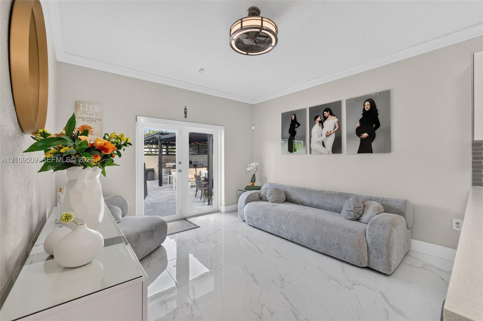 Polished tile flooring, crown molding, circular semi-flush mount lighting, and French doors leading to a paved patio area