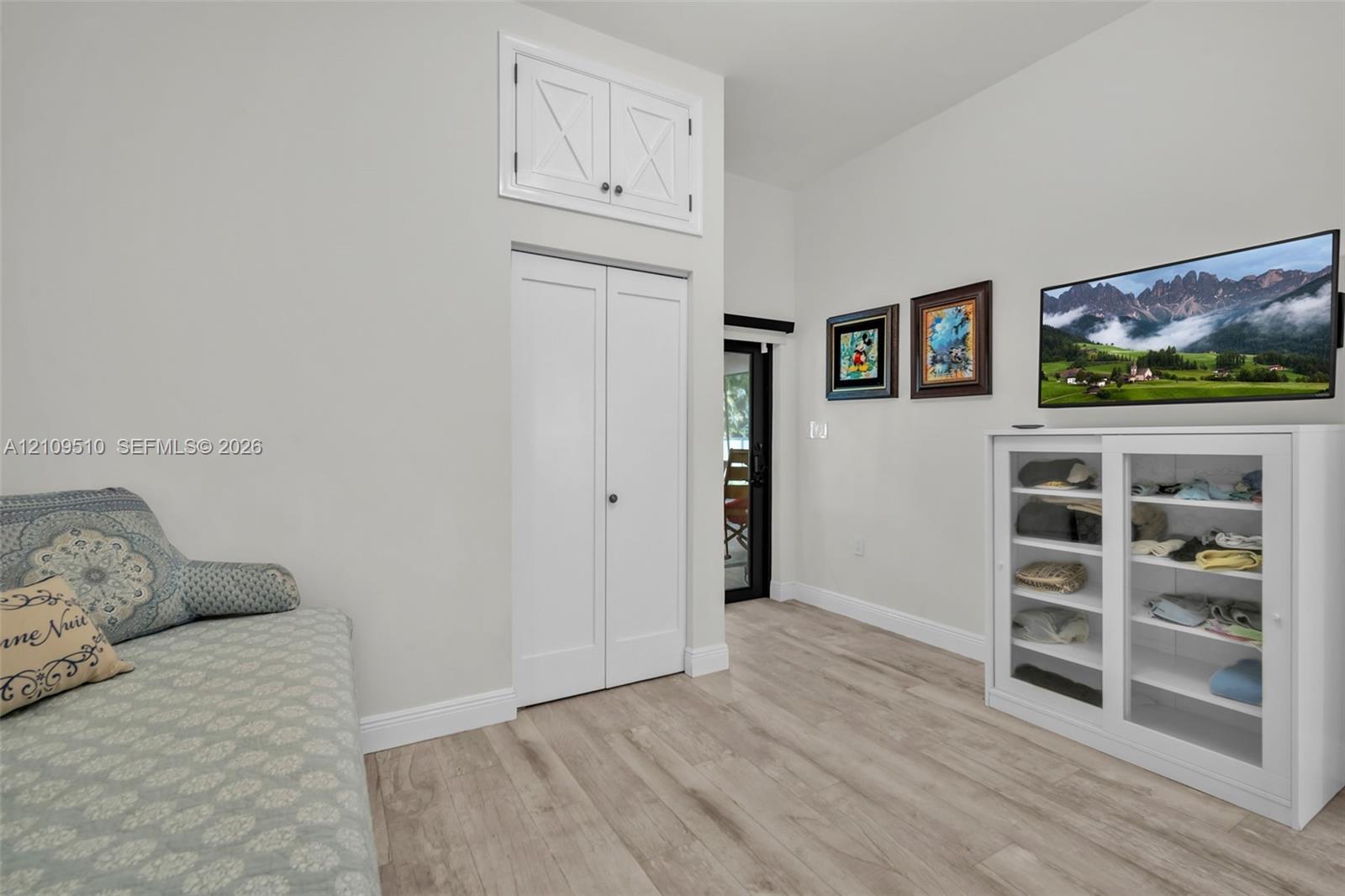 Wood-finish flooring, vaulted ceiling, dual-door closet, and upper storage cabinet with X-detail inlay