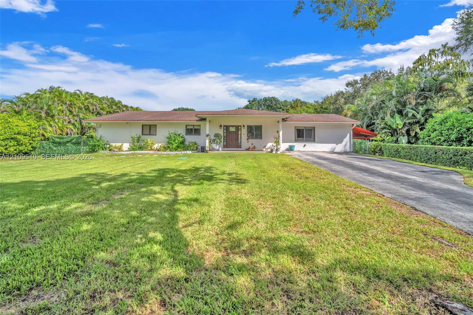 Single-story ranch exterior featuring a light-toned stucco faade, a covered entryway, a hipped shingle roof, and a paved driveway