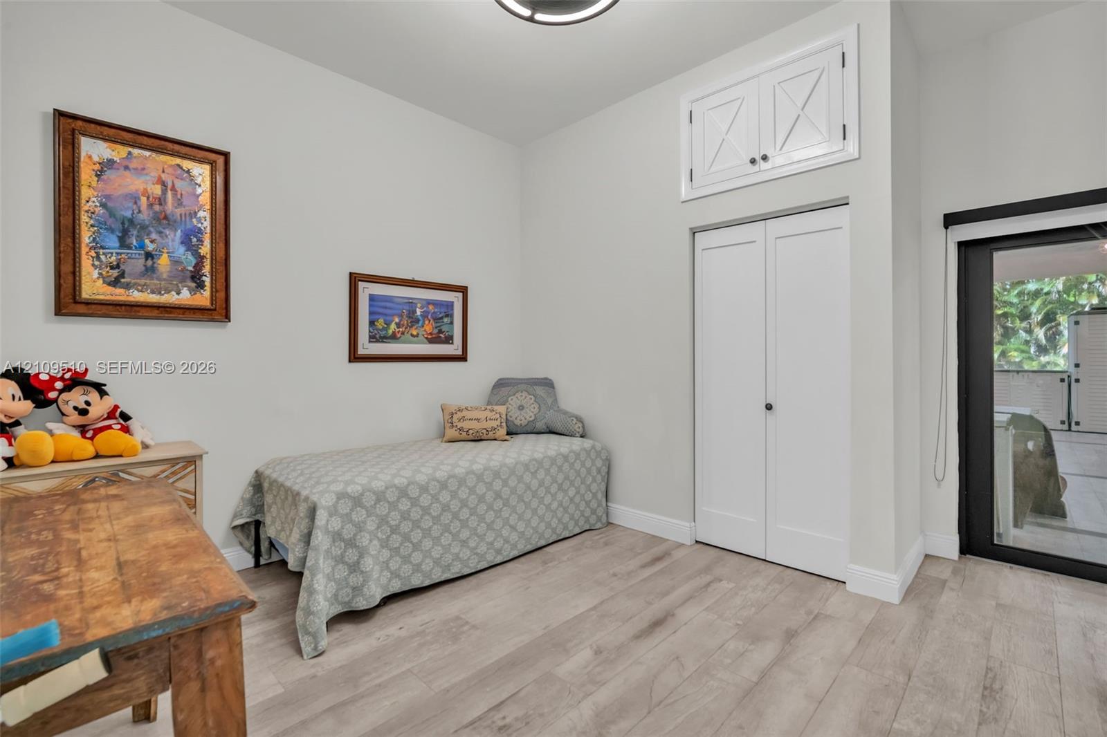 Room featuring wood-finish flooring, high ceilings, custom built-in upper storage, double-door closet, and glass-paneled exterior door with black framing