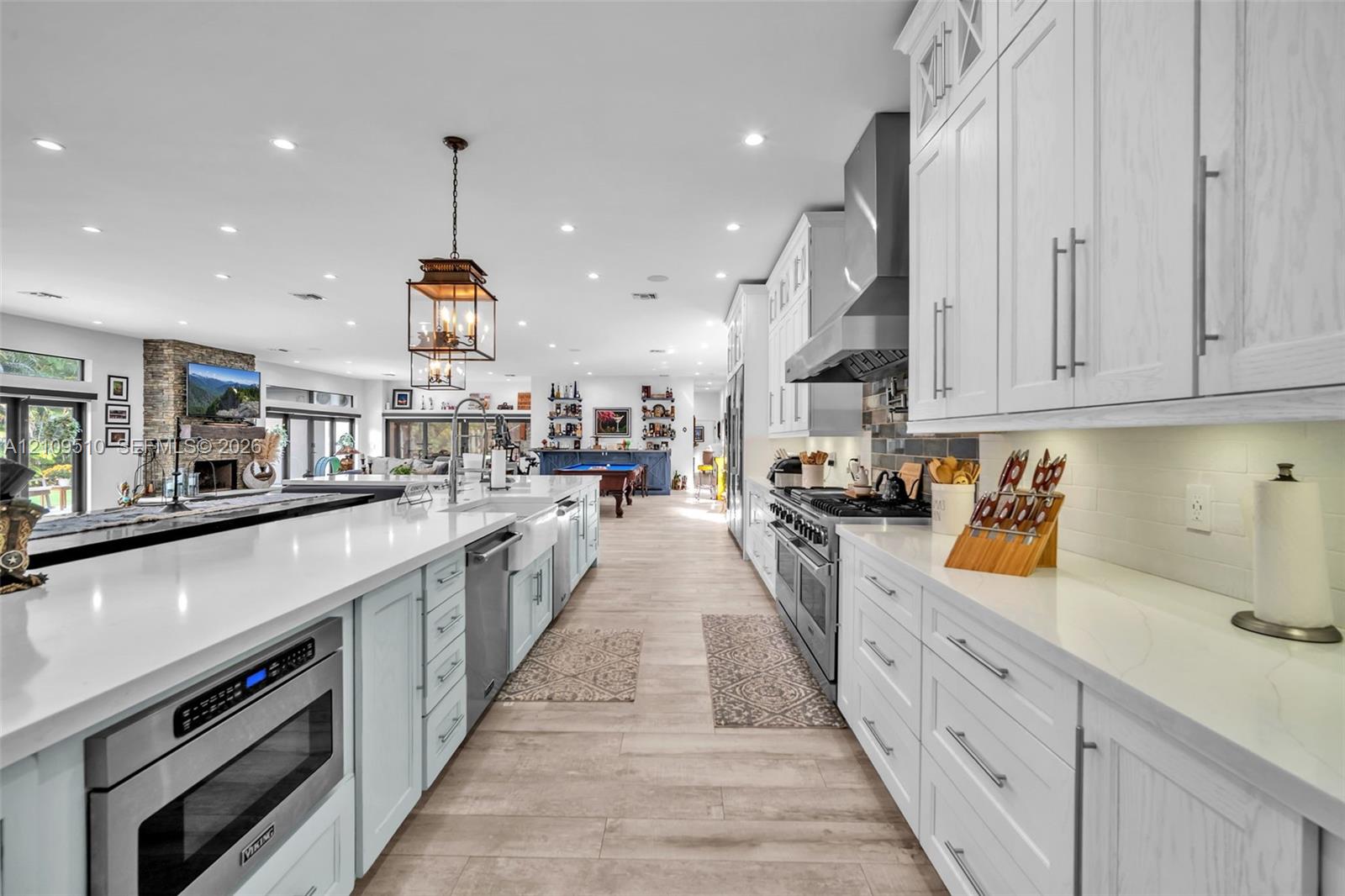 Kitchen featuring floor-to-ceiling white cabinetry, quartz countertops, a professional-grade stainless steel range with a matching hood, a farmhouse-style apron sink, and wood-finish flooring