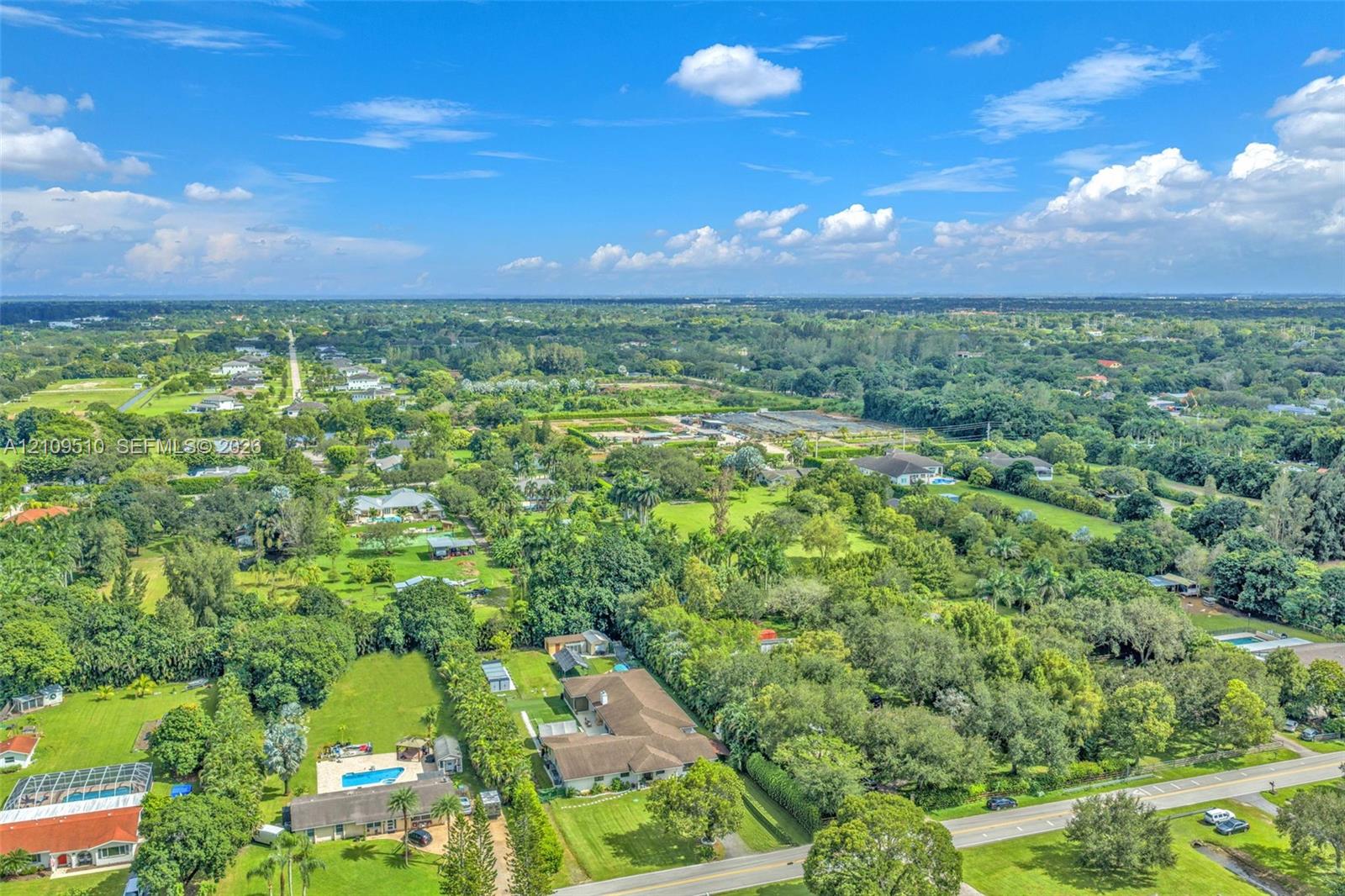 Aerial perspective of a sprawling residential property featuring a multi-gable roofline, a private in-ground swimming pool, extensive lawn space, and mature perimeter trees