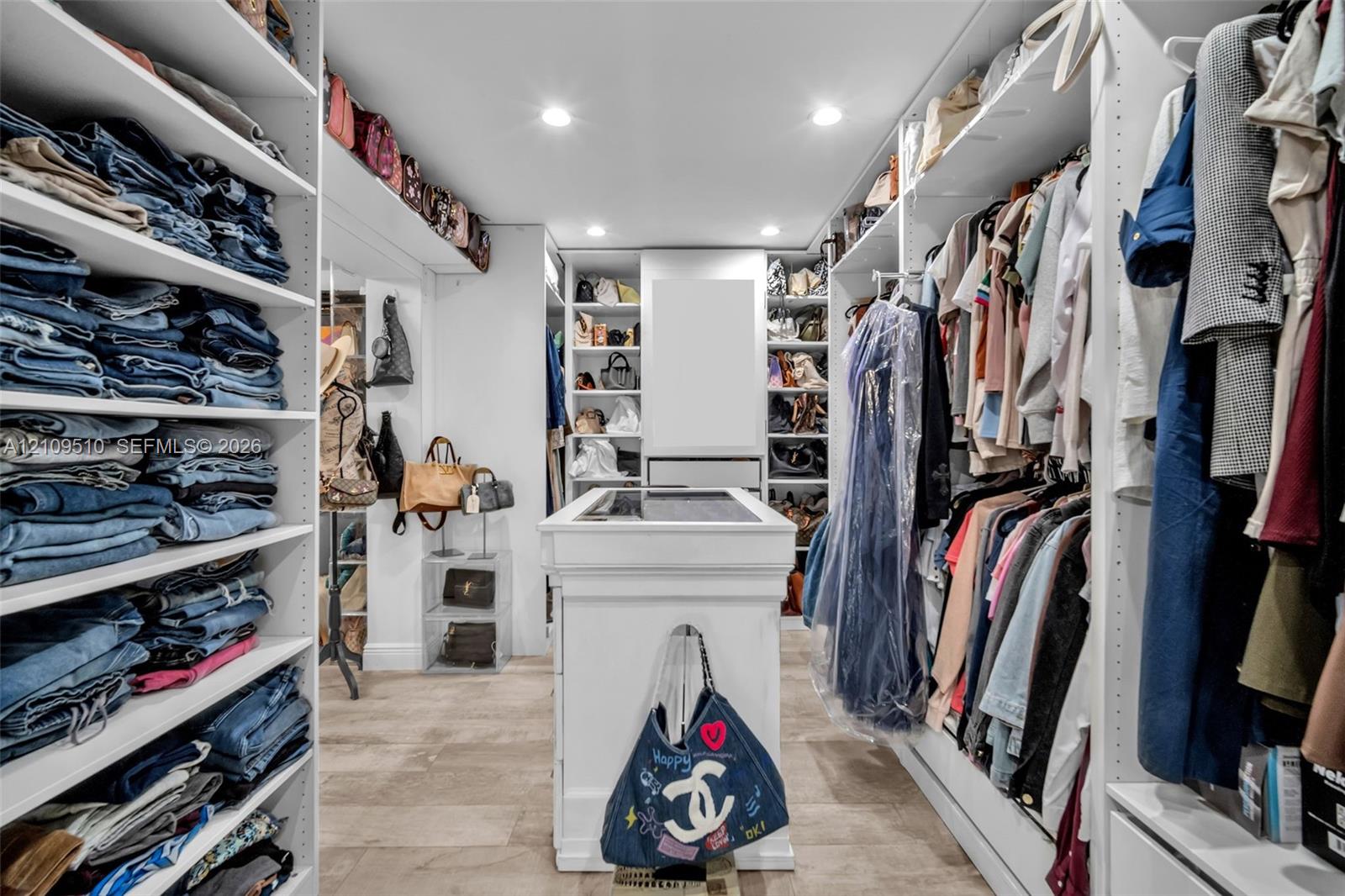 Walk-in closet featuring floor-to-ceiling white built-in shelving, a central storage island with a surface inlay, recessed lighting, and tile flooring