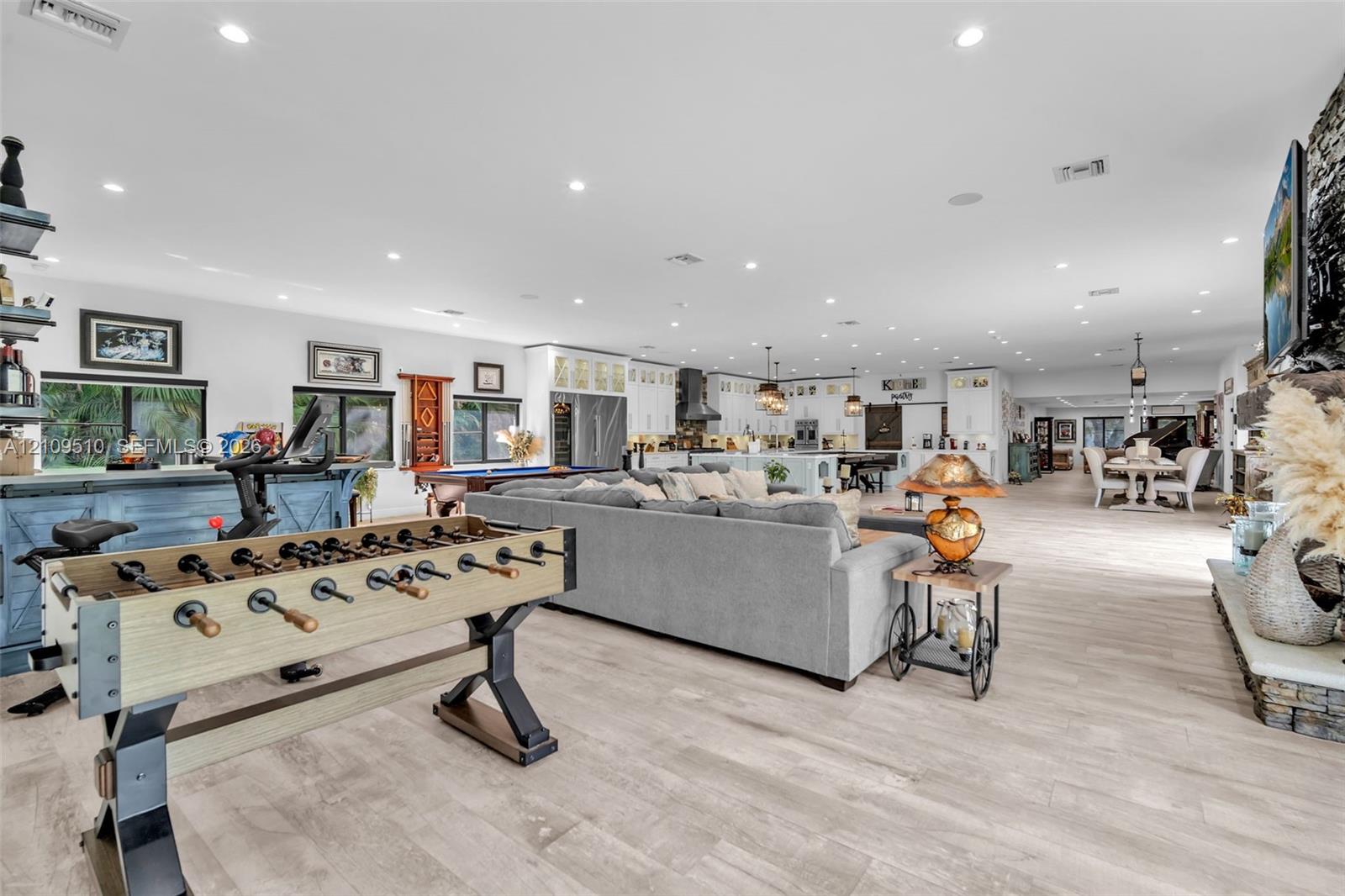 Open-concept interior featuring light wood-finish flooring, recessed lighting, a stone-accented fireplace hearth, and extensive custom cabinetry