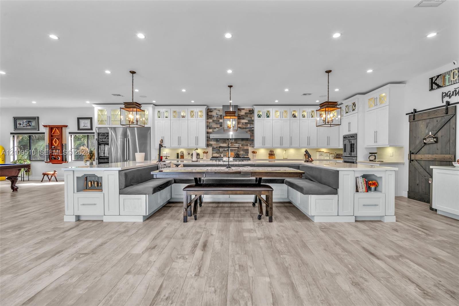 Kitchen featuring white cabinetry, wood-finish flooring, a stone-tiled backsplash, integrated banquet seating, and a sliding barn door