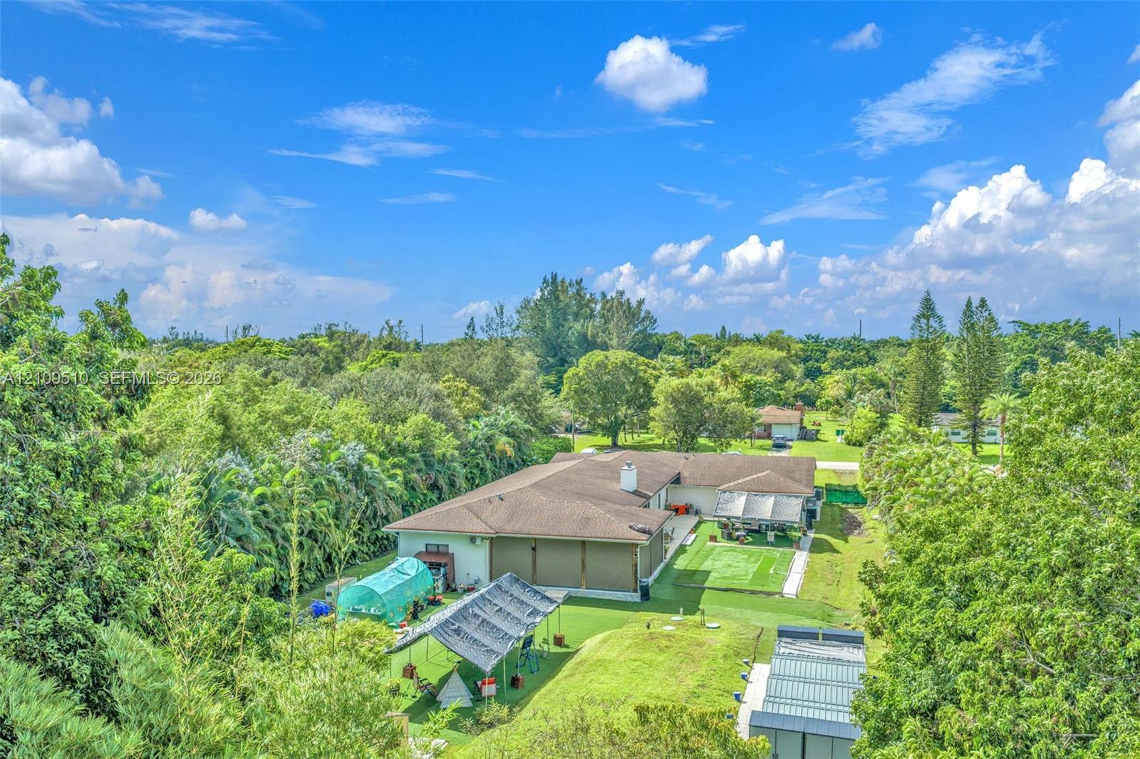 Single-story residence featuring a shingled roof, neutral-toned exterior, integrated covered patio, expansive lawn, and mature perimeter landscaping