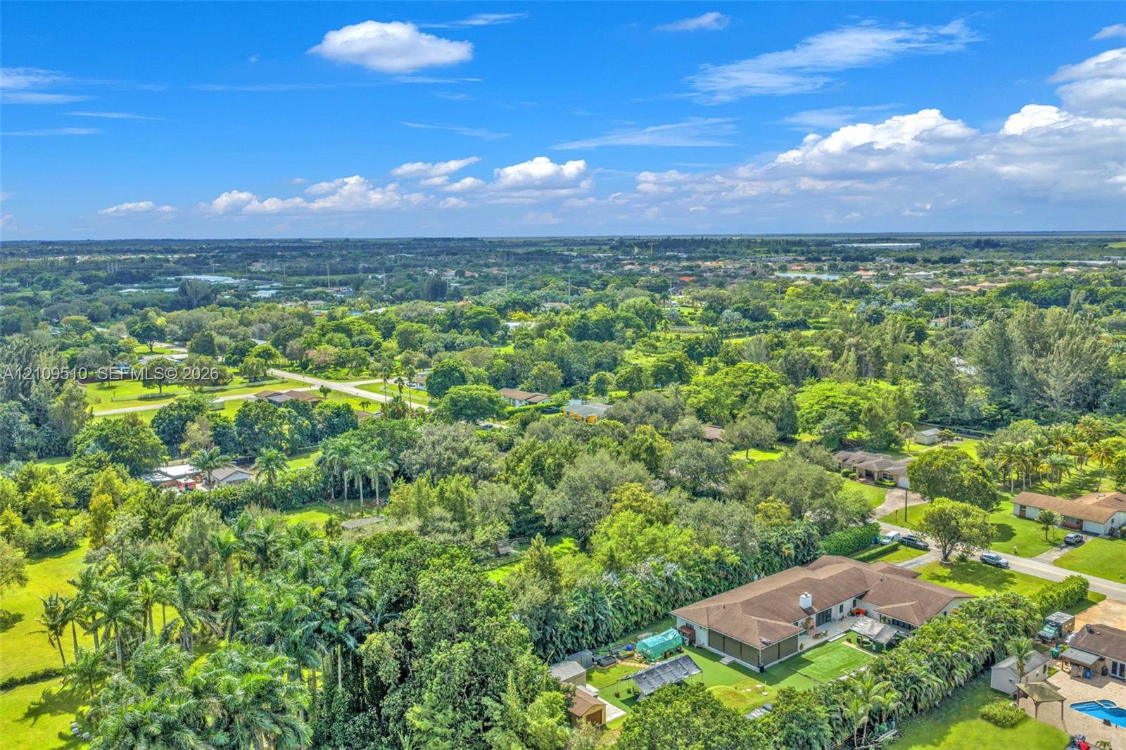 Aerial perspective of a sprawling property featuring mature trees, lush landscaping, a wide-reaching lot, and a residence with a multi-hipped roofline