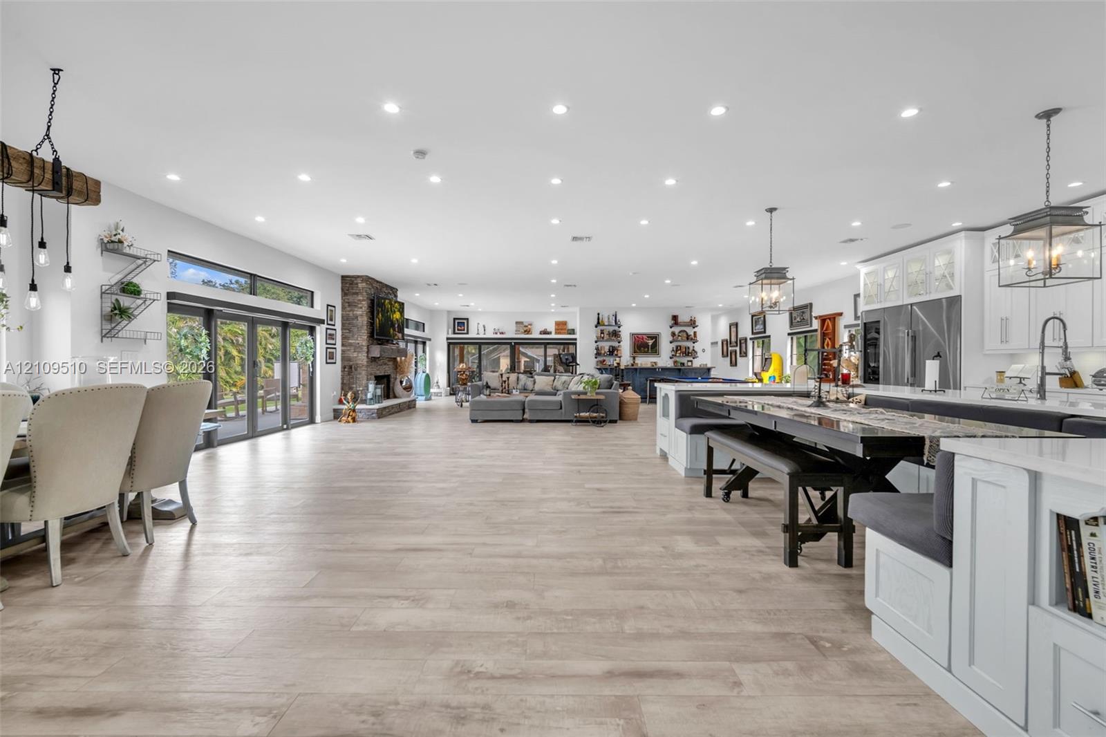 Open-concept interior featuring light wood-finish flooring, recessed lighting, stone-clad fireplace, and multi-panel folding glass doors