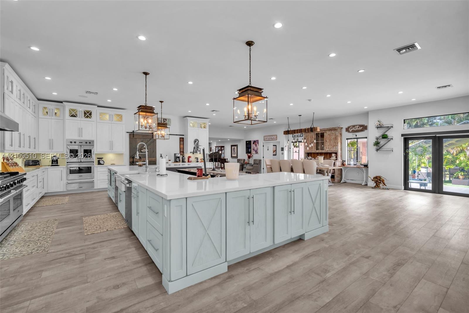 Open-concept kitchen featuring an expansive center island with stone countertops, white cabinetry, integrated stainless steel appliances, and wood-finish flooring throughout