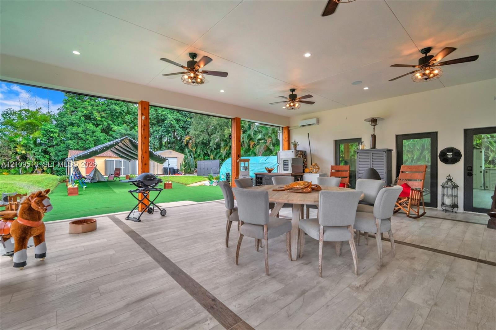 Covered outdoor patio featuring tile flooring with decorative inlay, exposed wood support beams, multiple ceiling fans with integrated lighting, and recessed ceiling lights