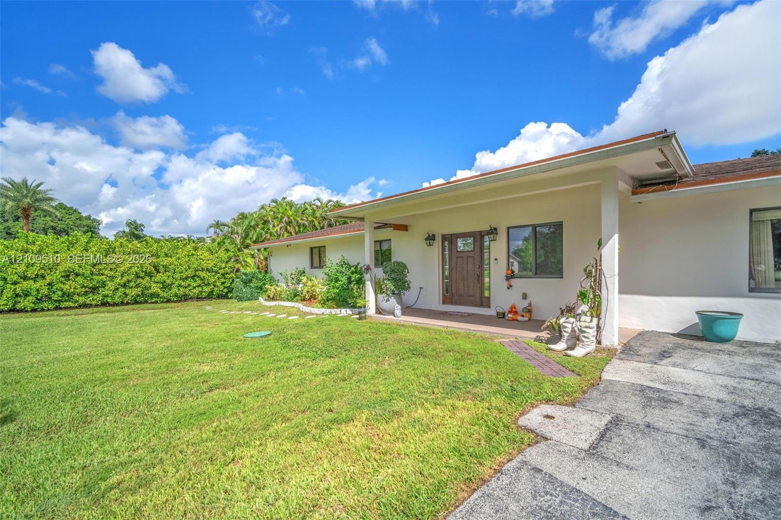 Single-story residence featuring a covered front porch, light-toned exterior finish, multi-pane entry door, concrete driveway, and expansive lawn area