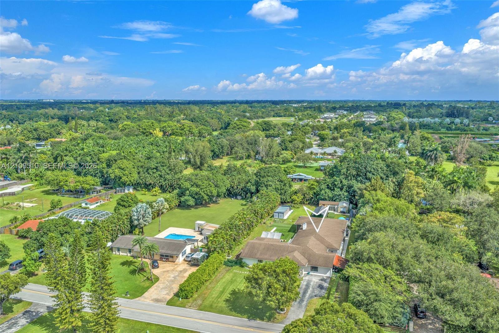 Aerial perspective of a detached residence featuring a multi-gabled roofline, concrete driveway, expansive lawn, and dense mature perimeter landscaping