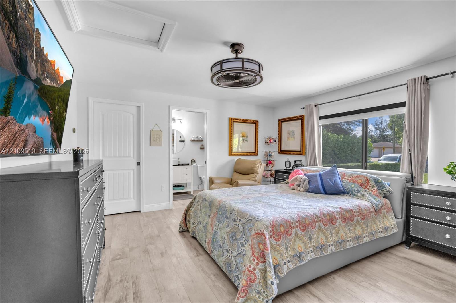 Light-filled bedroom featuring wood-finish flooring, a drum-style caged ceiling fan, and a wide window with integrated curtain rod hardware