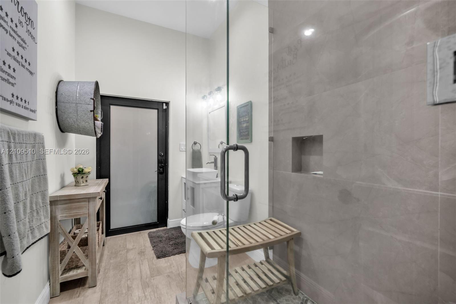 Walk-in shower featuring glass paneling, floor-to-ceiling tile surround, and a recessed soap niche, paired with wood-finish flooring and a frosted-glass exterior door