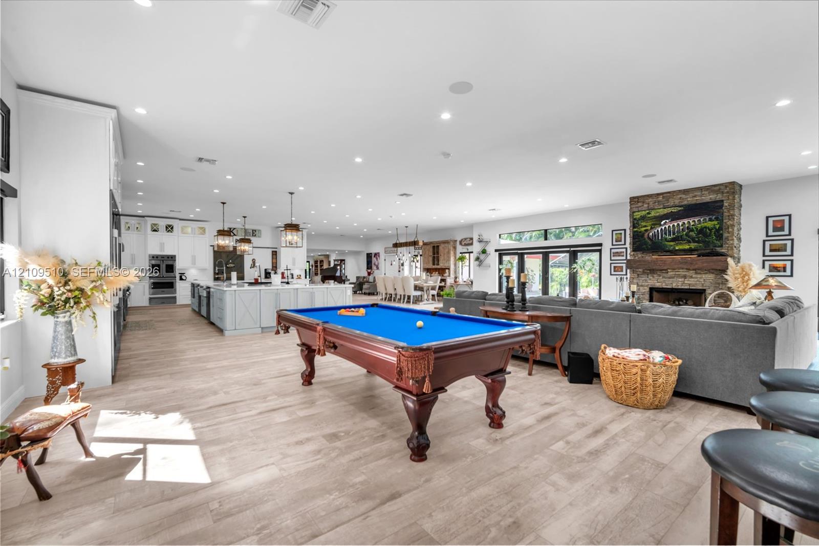 Open-concept interior featuring wood-finish flooring, recessed lighting, a stone-faced fireplace with a timber mantel, and a kitchen island with pendant lighting
