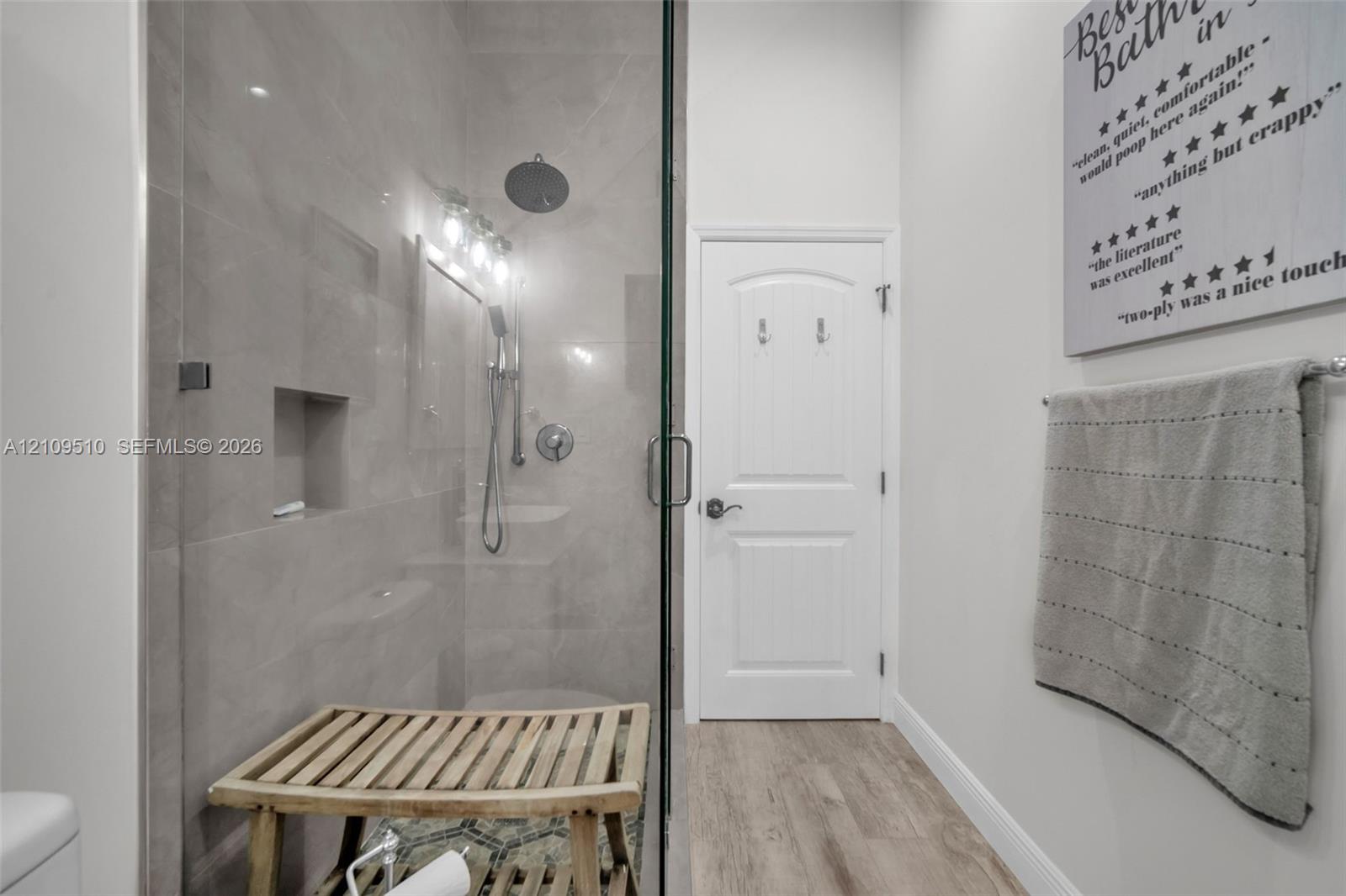 Walk-in shower featuring oversized tile walls, a recessed wall niche, a ceiling-mounted rainfall shower head, and a frameless glass door, complemented by wood-finish flooring