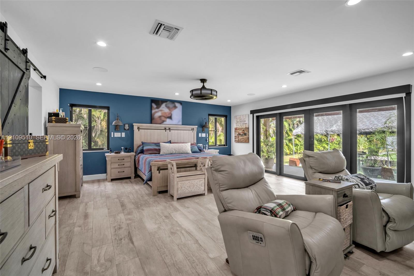Wood-finish flooring, accent wall, sliding barn door, recessed lighting, and multi-panel glass door system