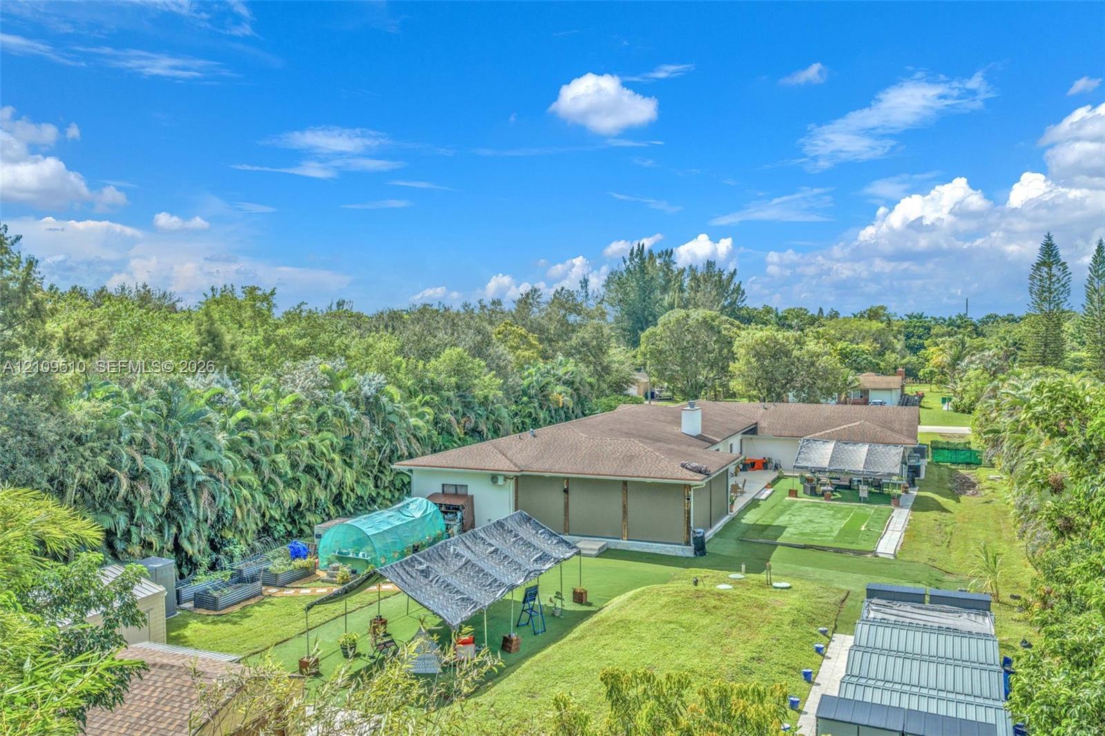 Expansive backyard featuring a sprawling lawn, mature perimeter trees, hardscaped patio, and multiple structural shade coverings