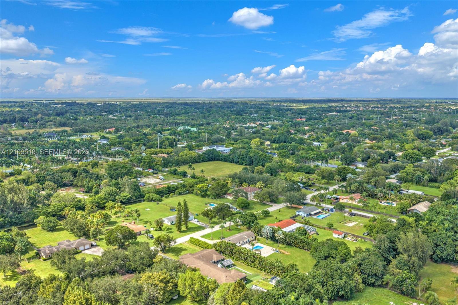 Aerial perspective of a sprawling residential landscape featuring expansive lots, mature greenery, and paved road access