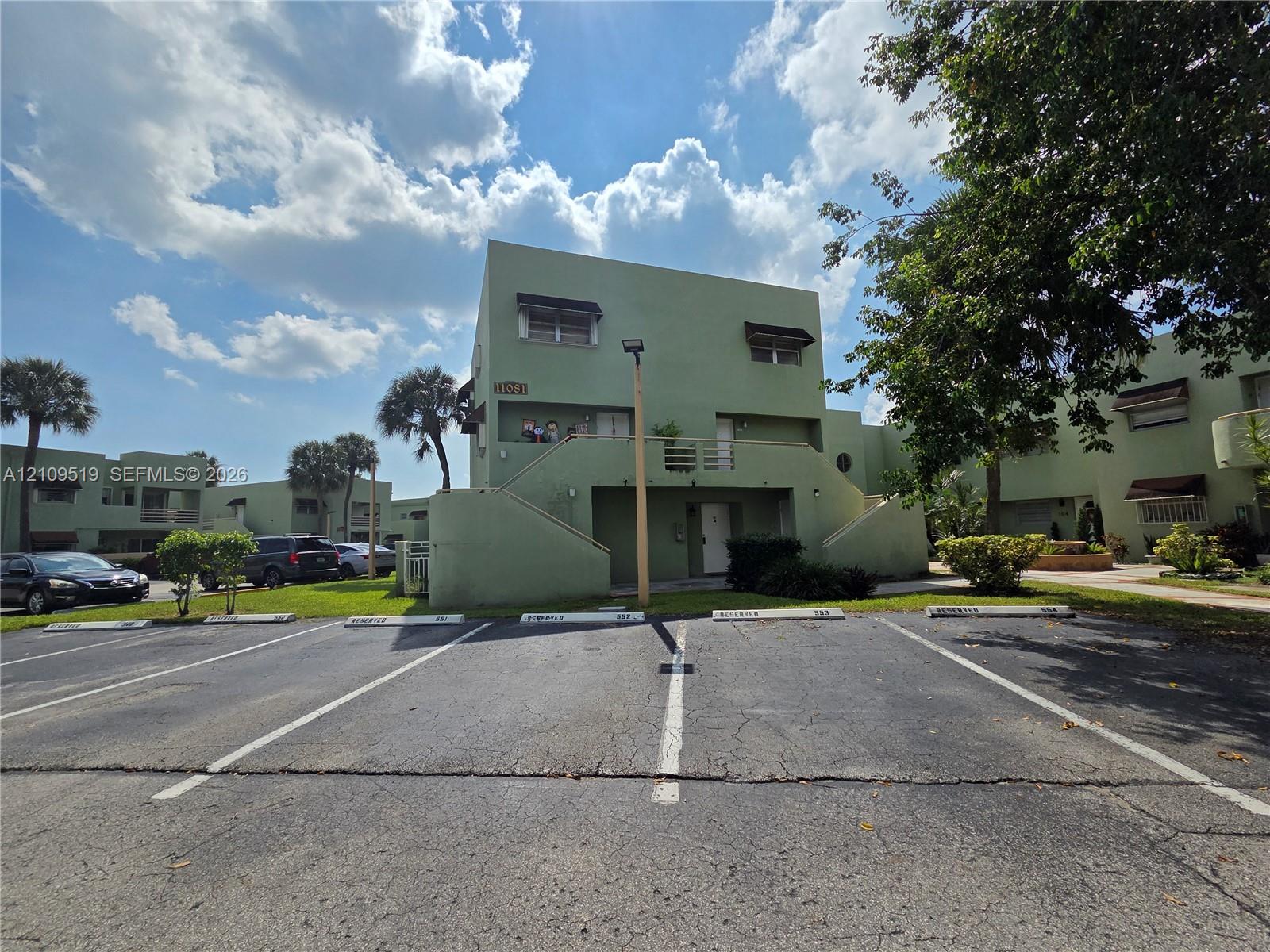 Exterior featuring a stucco facade, external staircase, individual assigned parking stalls, and mature landscaping