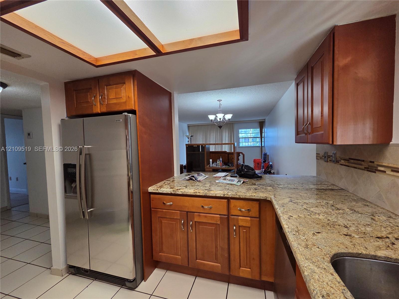 Kitchen featuring natural wood cabinetry, stone-surface countertops, stainless steel refrigerator, tile backsplash, and recessed ceiling lighting