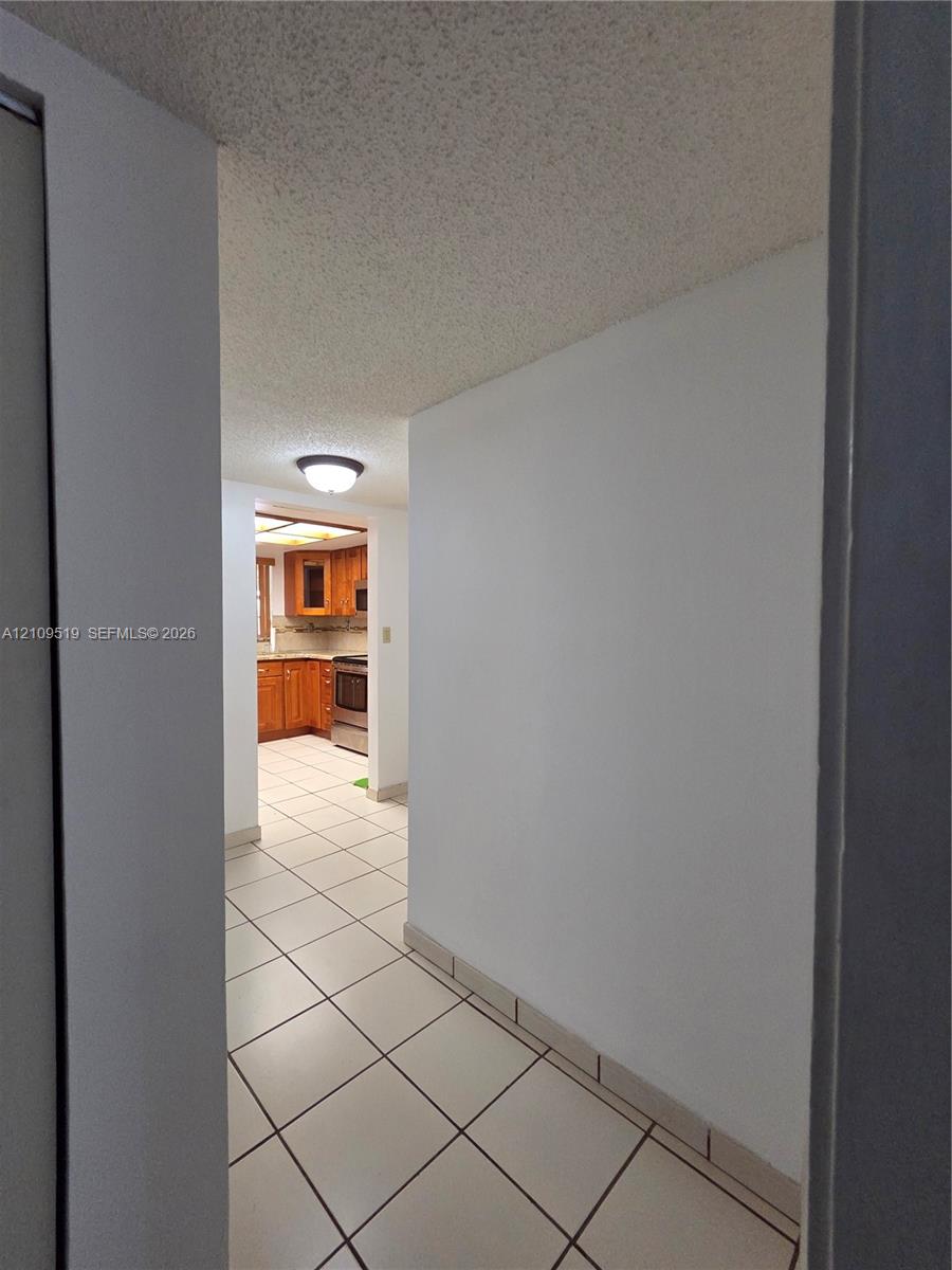 Ceramic tile flooring, flush-mount ceiling lighting, and wooden cabinetry with integrated appliances view from hallway