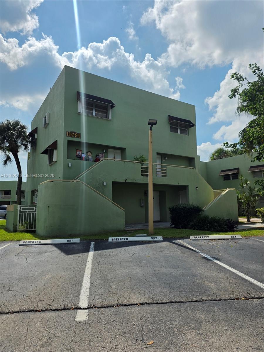 Unit encompasses entire ground floor of (3-story building) exterior featuring smooth stucco siding, designated parking spaces, concrete stairways, and protective window awnings