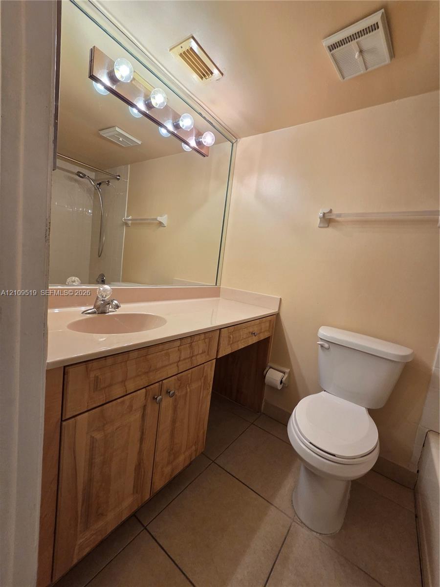 Bathroom featuring a vanity with wood-finish cabinetry, a solid-surface countertop, an integrated sink, a full-width wall mirror, and tiled flooring