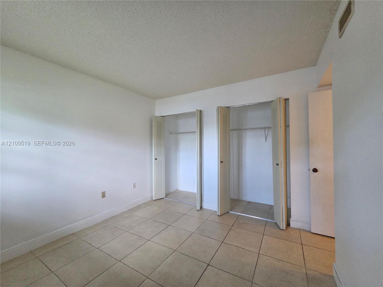 Room featuring neutral tile flooring, two closets with bi-fold doors, and a separate doorway entrance