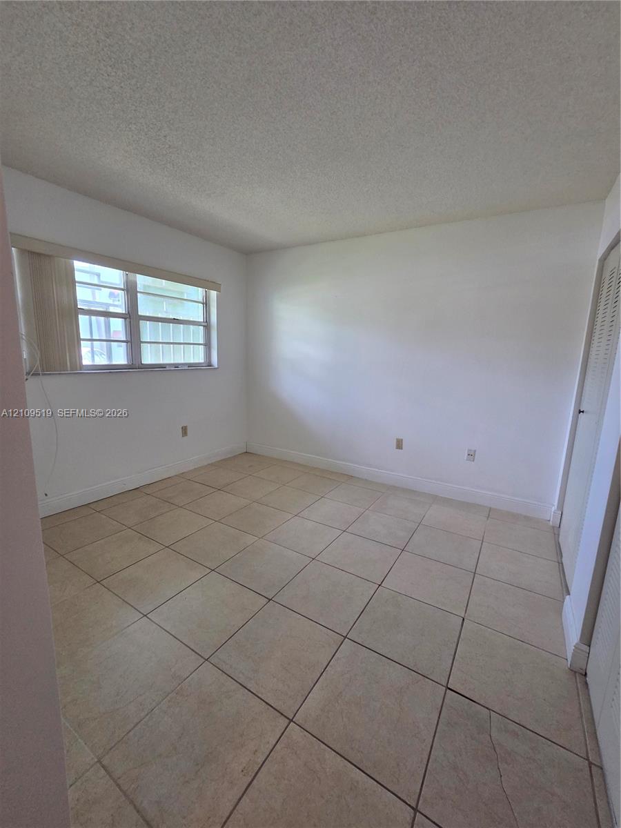 Interior room featuring neutral ceramic tile flooring, textured ceiling finish, and a window with horizontal blinds