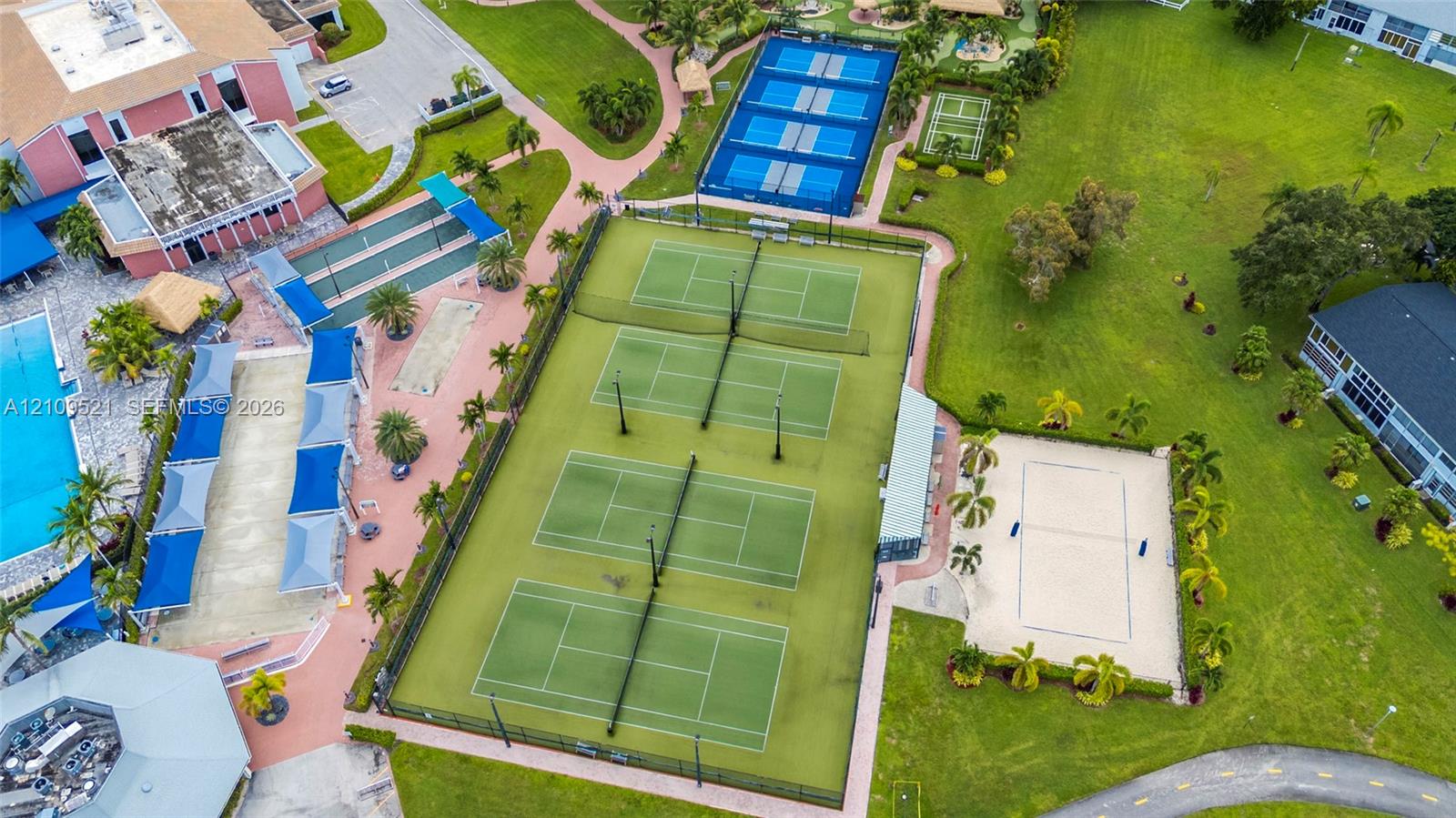 Recreational facility featuring four tennis courts, a sand court, blue-surfaced multi-use courts, and covered paved patio areas