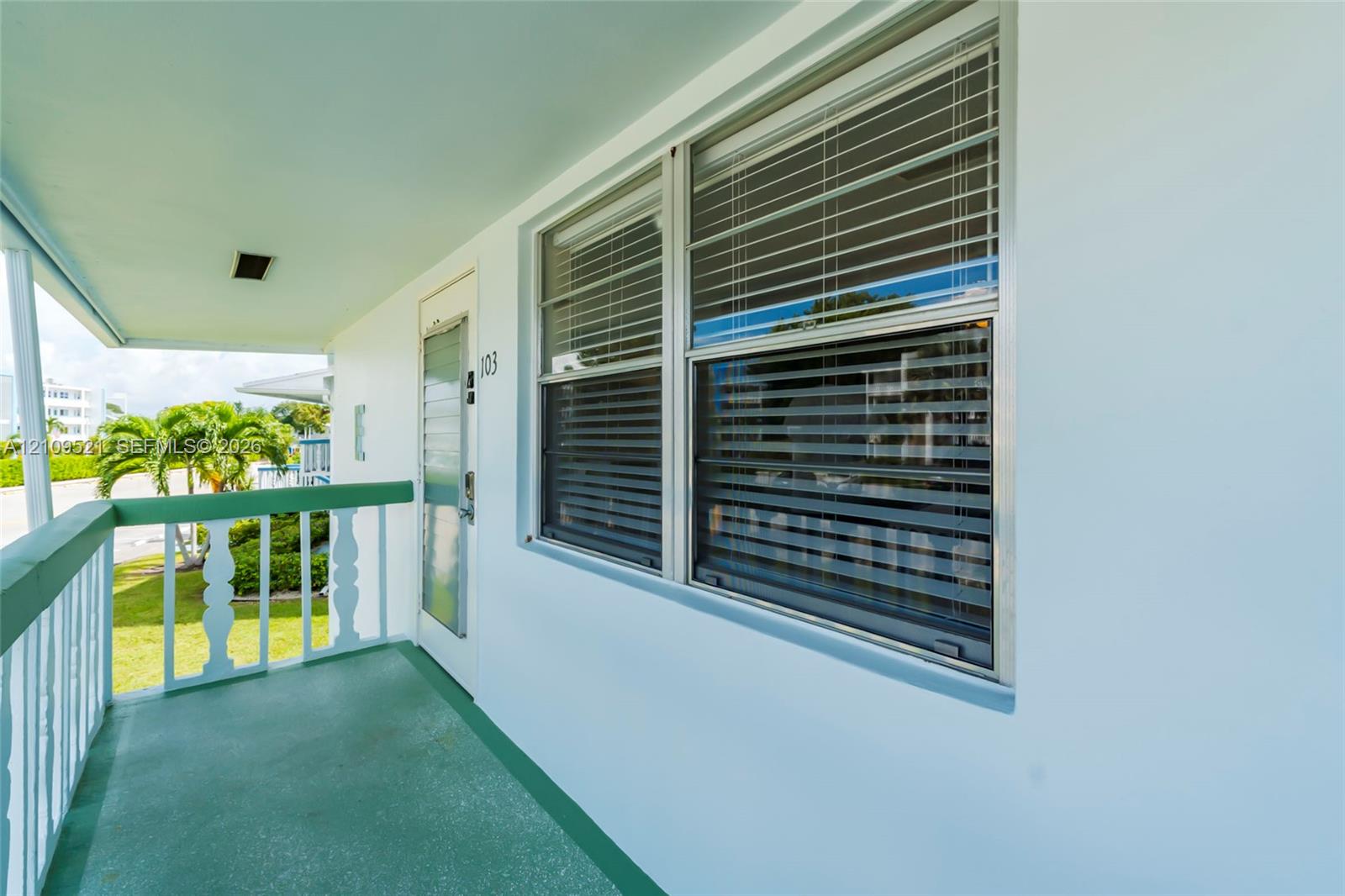 Covered exterior balcony featuring a solid-surface floor, painted railing with decorative posts, and horizontal sliding windows