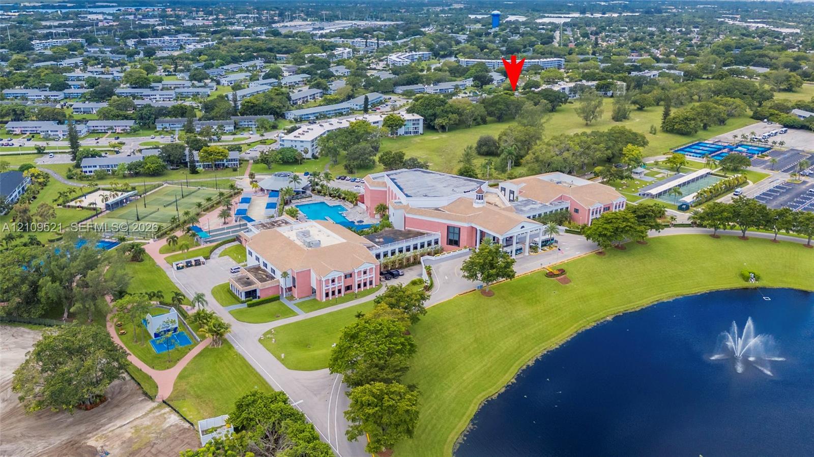 Aerial perspective featuring a multi-building complex, communal swimming pool, tennis courts, and a central water feature with a fountain
