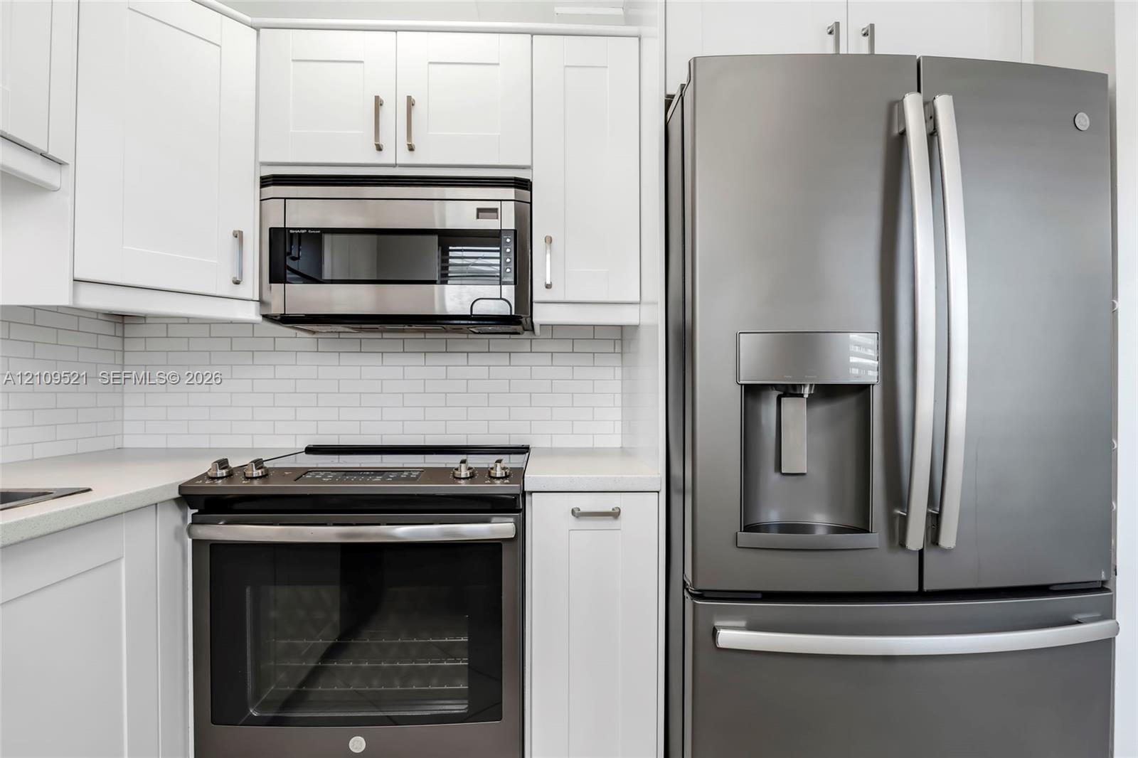 White shaker-style cabinetry, stainless steel microwave, matte-finish range, French-door refrigerator, and white subway tile backsplash