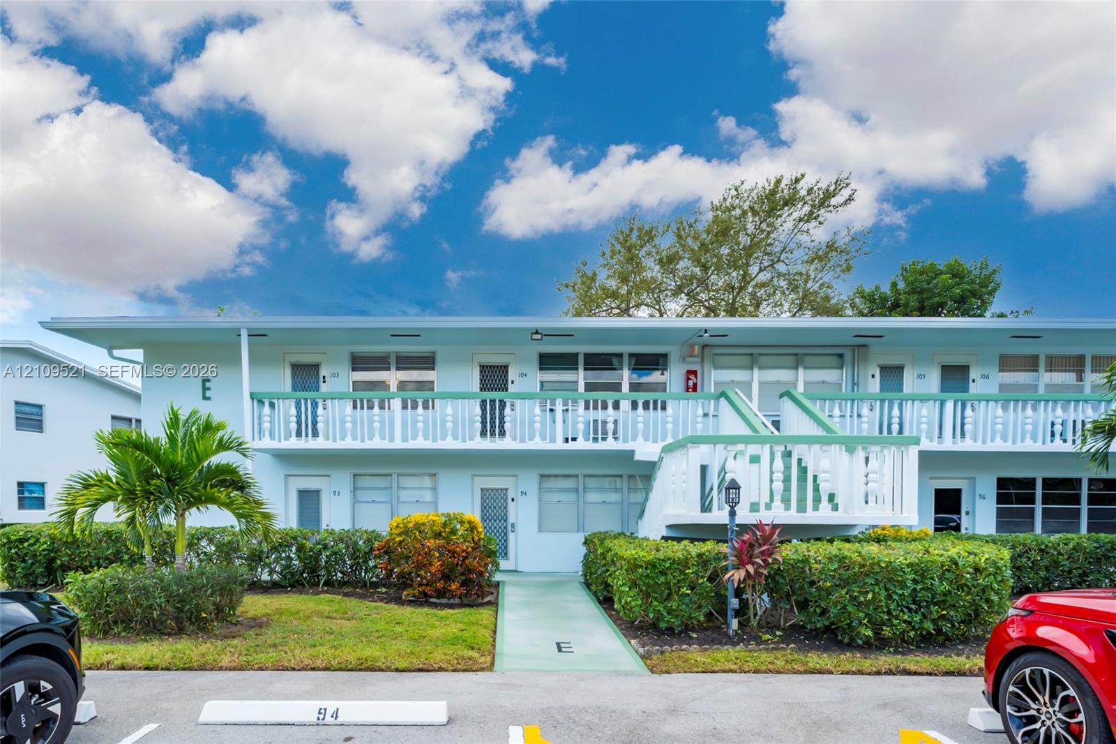 Two-story building exterior featuring a second-level balcony with white balustrades, horizontal window configurations, exterior stair access, and manicured shrubbery Two-story building exterior featuring a second-level balcony with white balustrades, horizontal window configurations, exterior stair access, and manicured shrubbery