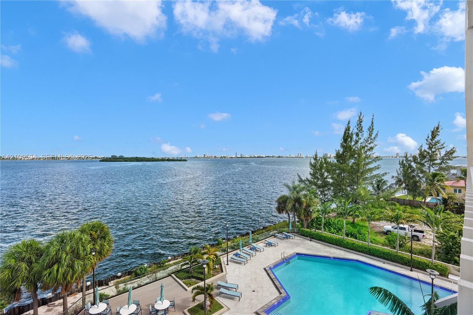 Outdoor swimming pool with tile decking and stone-paver surroundings, bordered by manicured landscaping and mature palm trees, featuring an expansive water view Outdoor swimming pool with tile decking and stone-paver surroundings, bordered by manicured landscaping and mature palm trees, featuring an expansive water view