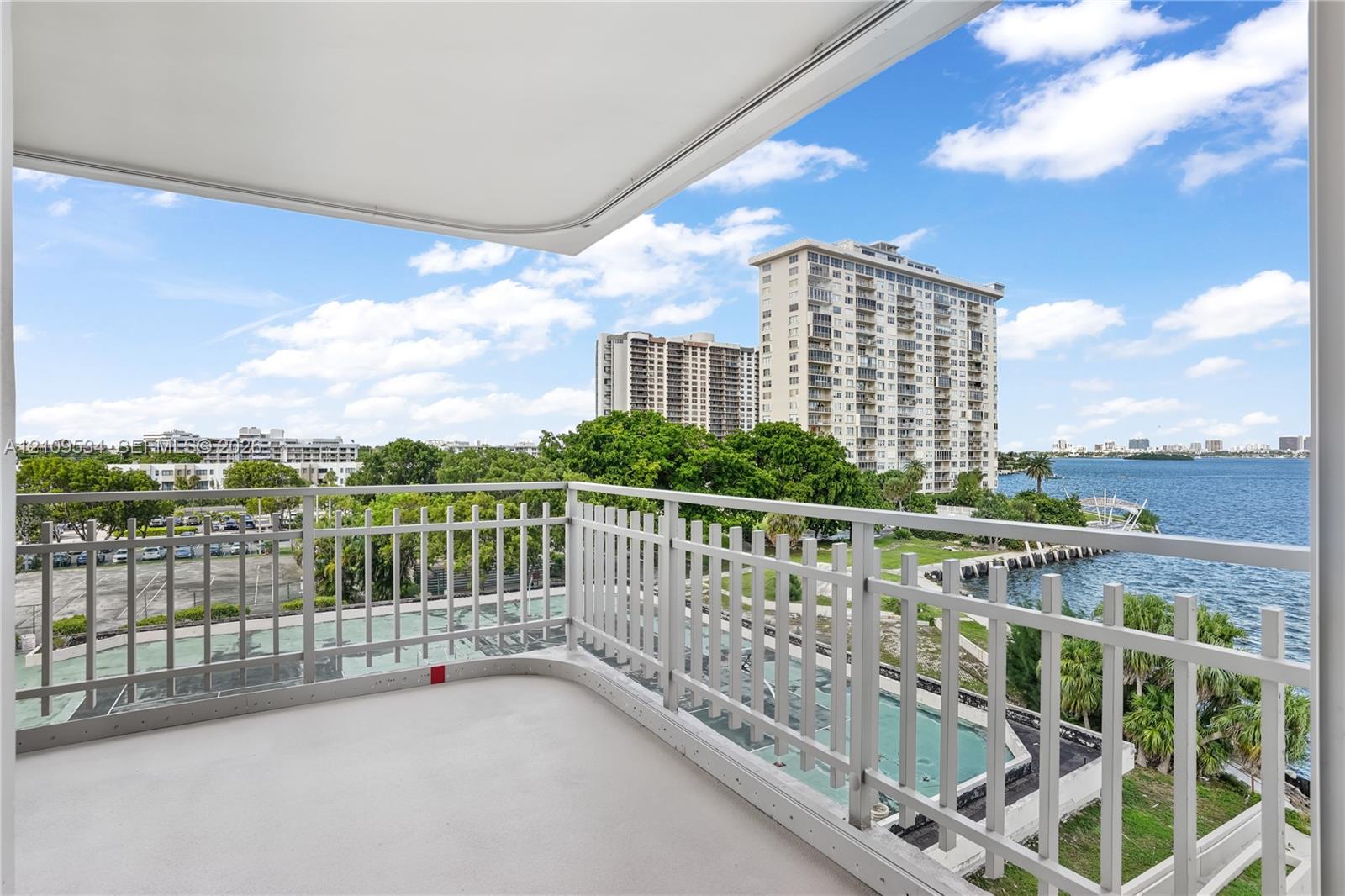 Covered balcony featuring white metal railings and concrete flooring, overlooking the waterfront