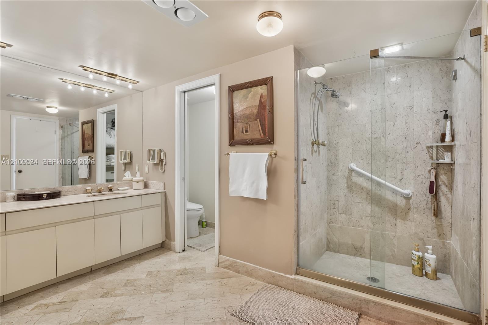 Bathroom featuring a dual-sink vanity with countertop, large wall-to-wall mirror, and stone-tile flooring