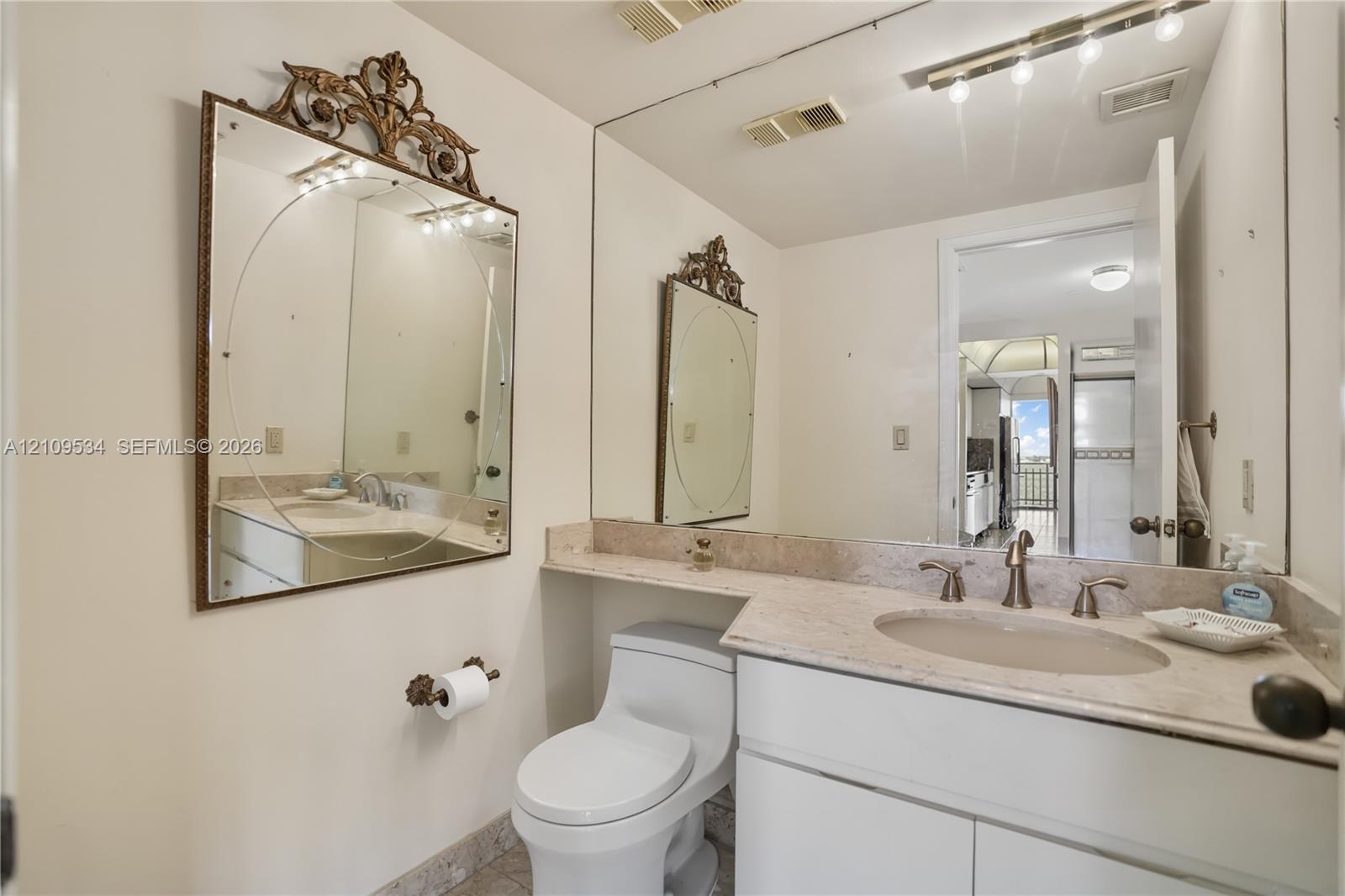 Bathroom featuring a stone-topped vanity with an integrated basin, white cabinetry, a large wall-mounted mirror, and an overhead vanity light fixture